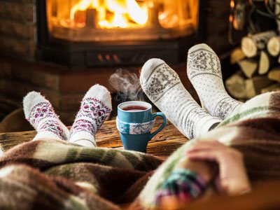 Zwei Menschen wärmen sich mit Woll-Socken am Kaminfeuer